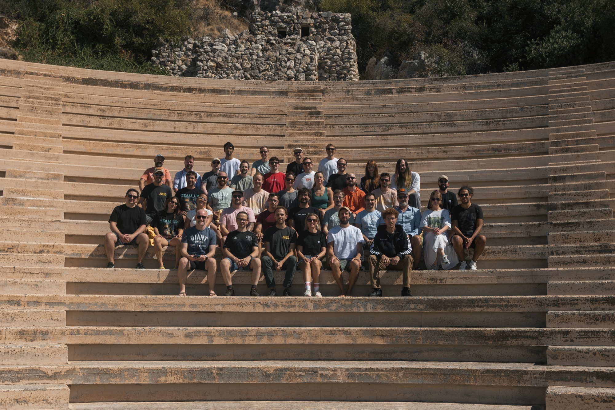 The Giant Swarm team sitting together on the stone steps of an open-air amphitheatre at our annual offsite in Greece